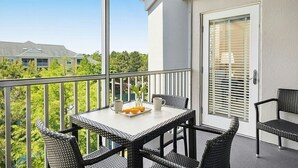 A balcony with wicker furniture, a table with a tray of oranges and a cup, and a door with blinds.