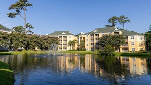 A multi-story hotel with a central courtyard featuring a fountain, surrounded by lush greenery and trees.