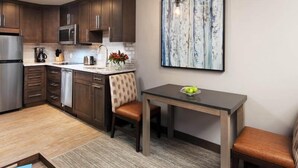 Una cocina moderna con armarios de madera oscura, un refrigerador de acero inoxidable y un microondas. Hay una mesa de comedor con dos sillas y un jarrón con flores.