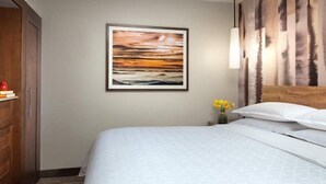 Habitación de hotel con cama, armario de madera, un cuadro enmarcado, un jarrón con flores amarillas y un cabecero con panel de madera vertical.