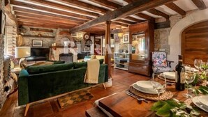 A rustic interior with exposed wooden beams, a green sofa, a dining table set with plates and glasses, and a fireplace. - El Jardín Escondido - country house in Helgueras (Cantabria) | 12 guests (Helgueras)
