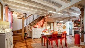A dining area with a wooden table and chairs, a staircase, and a kitchen in the background. - El Jardín Escondido - country house in Helgueras (Cantabria) | 12 guests (Helgueras)