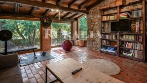 A rustic room with a brick floor, wooden ceiling beams, a large window, a bookshelf, and exercise equipment. - El Jardín Escondido - country house in Helgueras (Cantabria) | 12 guests (Helgueras)