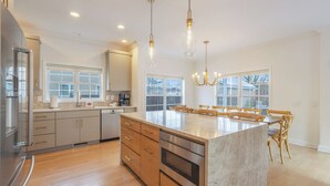 A modern kitchen with a large island, stainless steel appliances, wooden cabinets, and a dining area with chairs. - 5 O'clock Somewhere - large home, hot tub & close to the beach! (South Haven)