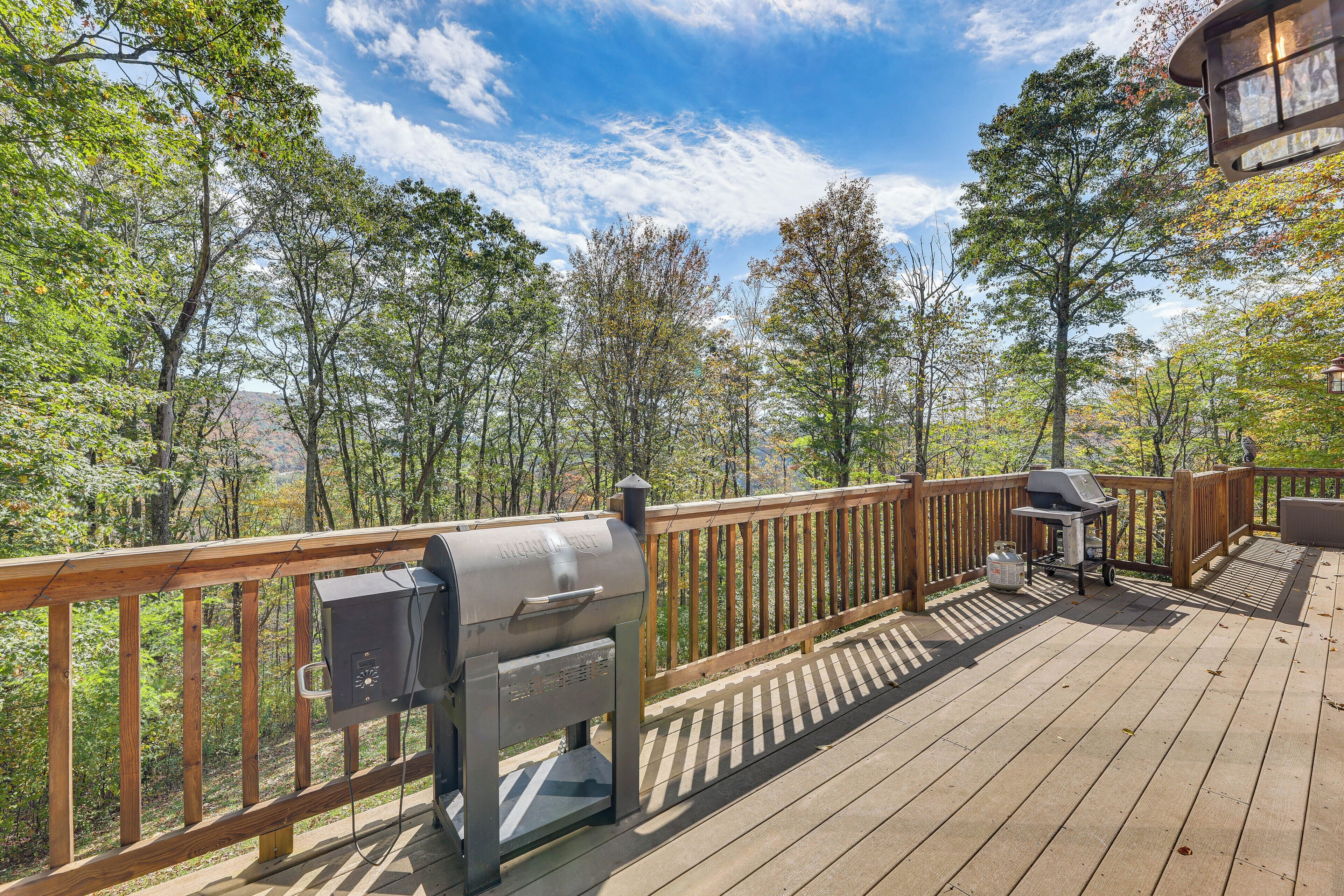 A deck with a grill and a grill cart, surrounded by a wooden railing and trees.