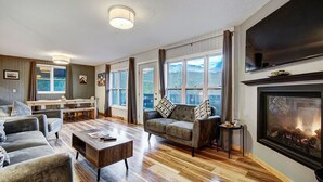 A spacious living room with a fireplace, wooden flooring, and a large window overlooking a scenic view. - The Apres Chalet on Peak 7, Private Hot Tub, Locaton & Great Views! (Breckenridge)
