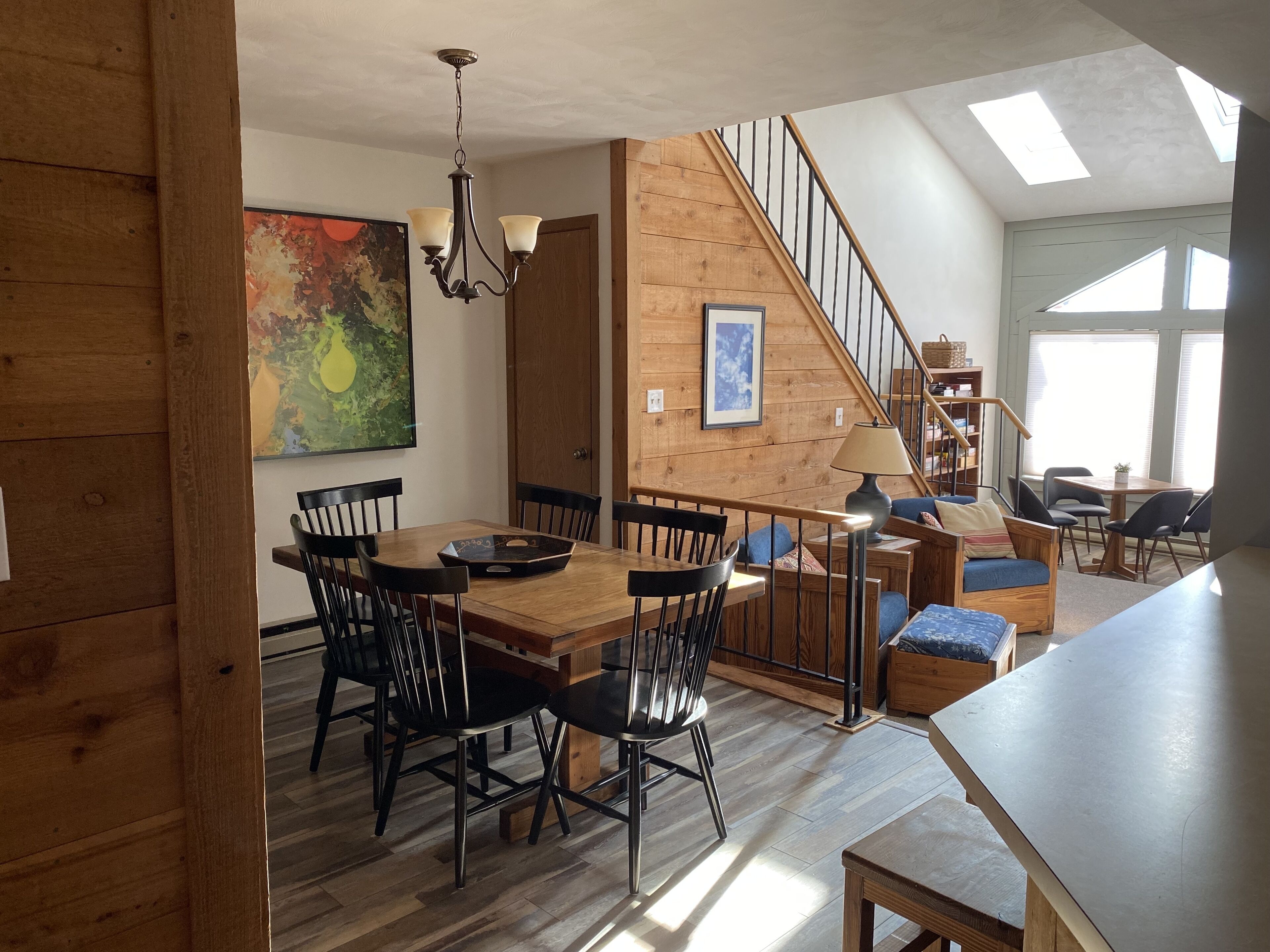 A spacious dining area with a wooden table and chairs, a chandelier, and a staircase leading to an upper level.