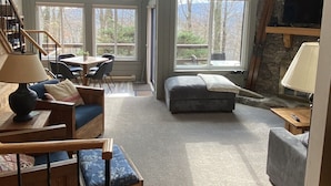 Ein geräumiges Wohnzimmer mit hoher Decke, Dachfenstern, einer Steinwand und großen Fenstern mit Blick ins Freie.