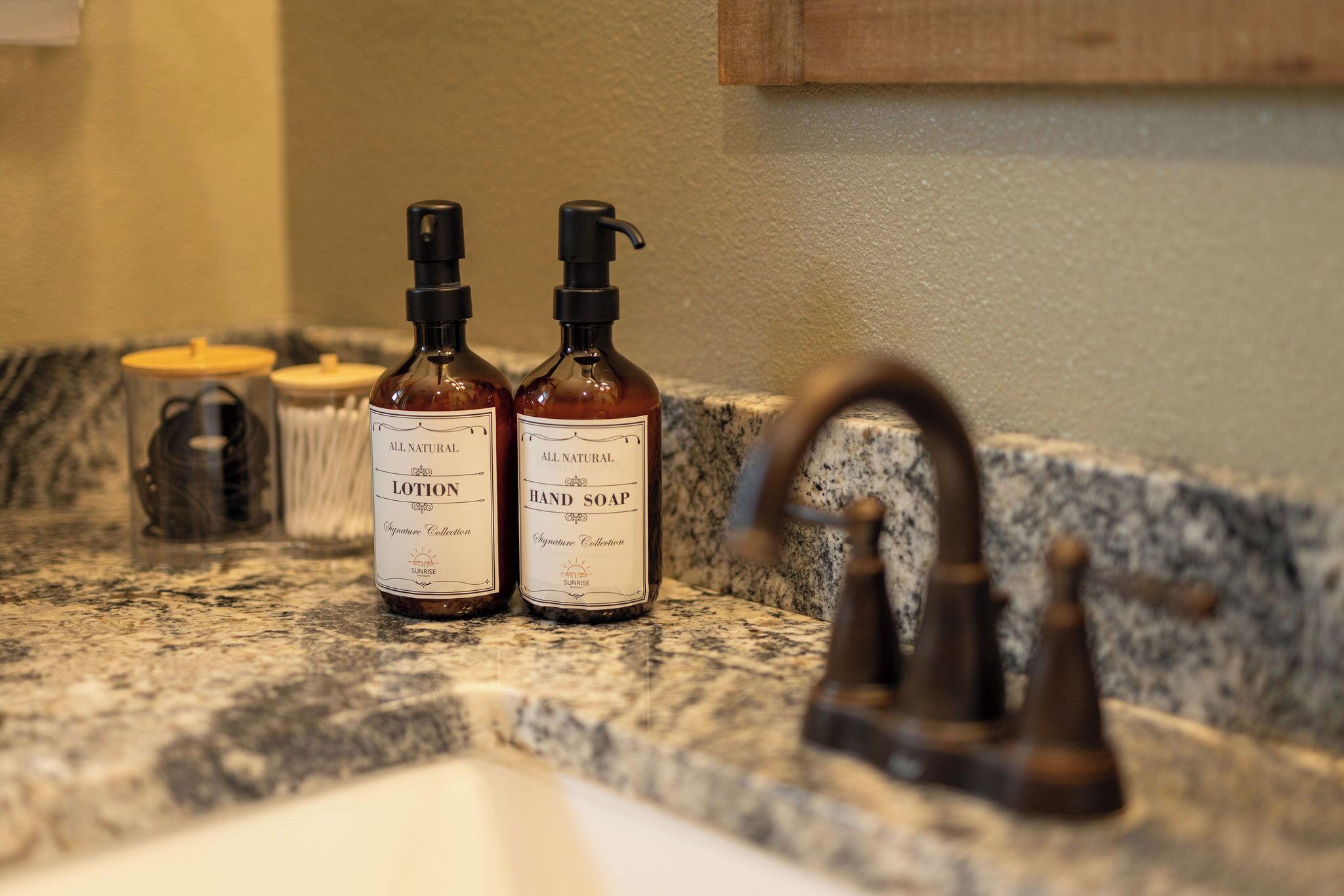 Deux flacons de lotion et un savon pour les mains sont posés sur un plan de travail en granit, près d’un évier.
