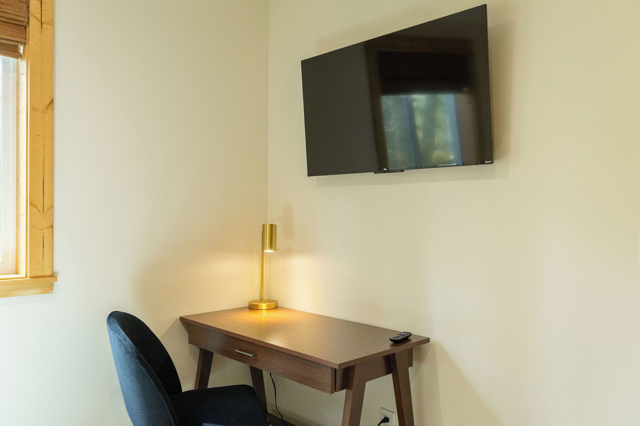 Ein kleiner, ordentlicher Arbeitsplatz mit Schreibtisch, Stuhl und einem Wand-Fernseher.