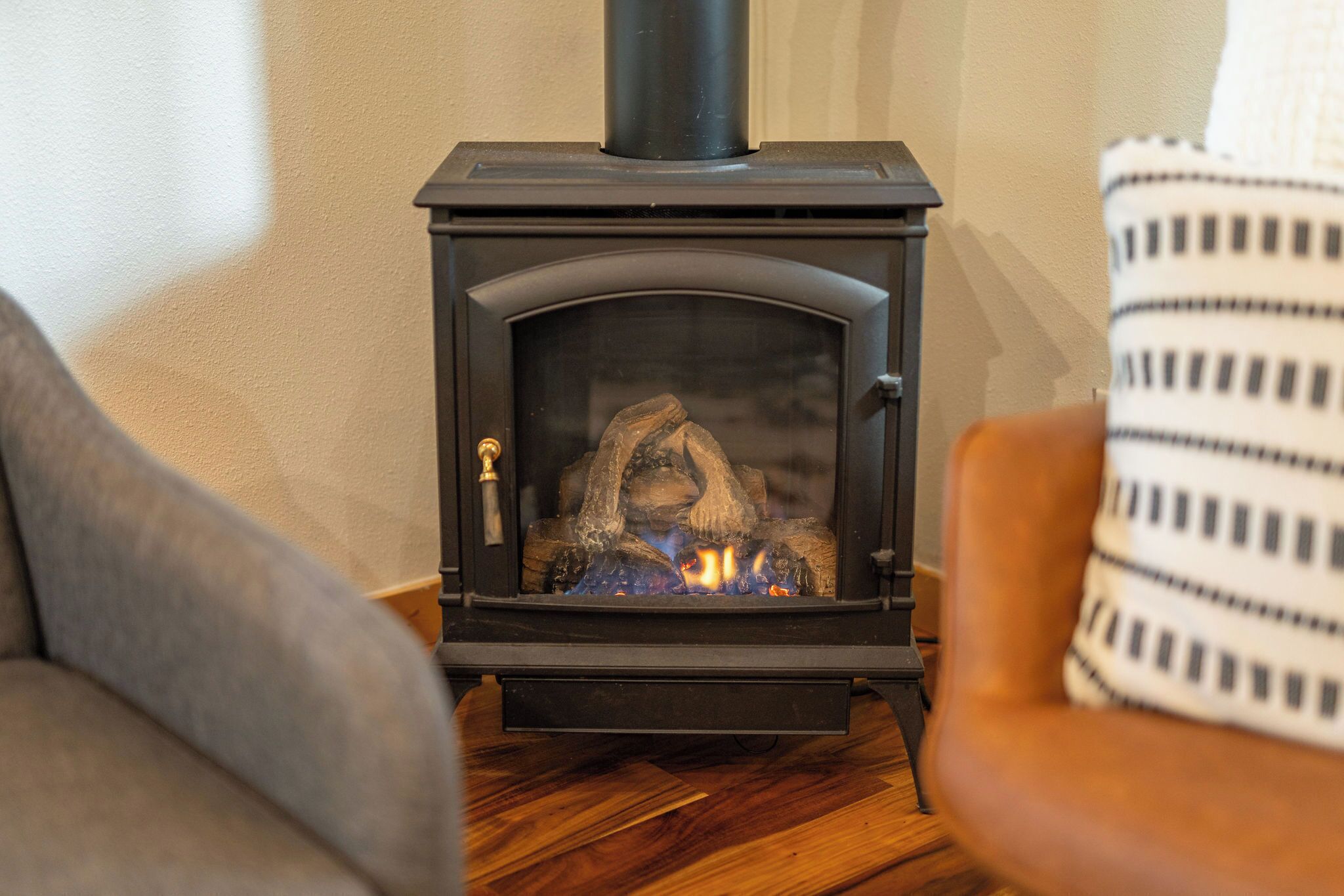 A wood-burning stove in a living room with a sofa and a patterned cushion.