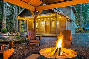 A cozy cabin with a fire pit, wooden deck, and a covered porch with string lights. - Relax by Rainier: Cozy Luxe King, Full Kitchen, Covered Fire Pit, 5 mi to Park (Ashford)