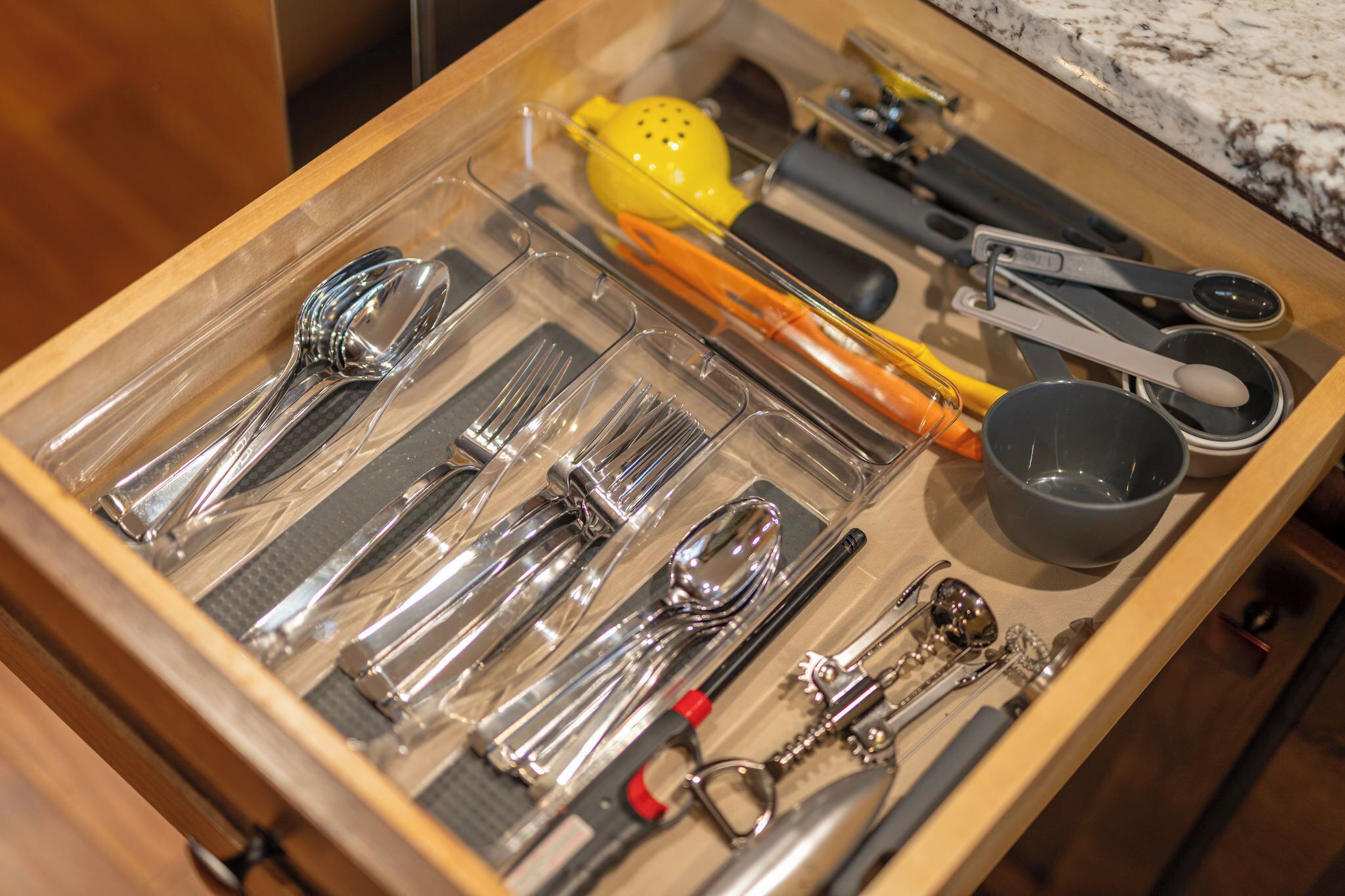 Un cajón con varios utensilios de cocina ordenados, como cucharas, una cuchara grande y tazas medidoras.