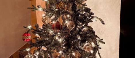 A Christmas tree with lights and ornaments, placed on a wooden floor near a staircase.