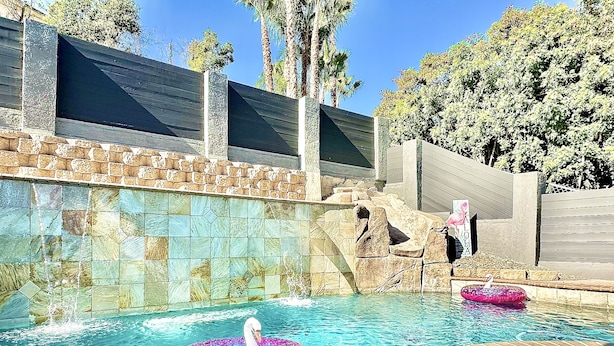 A swimming pool with a swan float and a flamingo float, surrounded by stone walls and palm trees. - Sleeps 50+ NEW Luxury Private Resort with Pool Golf Arcade Spa Playground Poker (Lakeside)