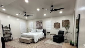 A modern bedroom with a large bed, two ceiling fans, a small round table, a black armchair, and a potted plant. - Sleeps 50+ NEW Luxury Private Resort with Pool Golf Arcade Spa Playground Poker (Lakeside)