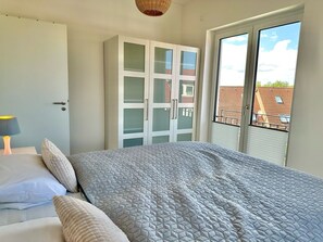 Un dormitorio con cama, armario y ventana con vistas a edificios.