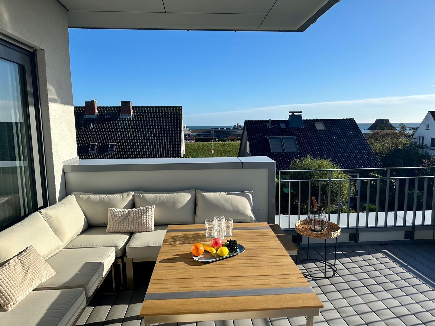 Un balcón con un sofá, una mesa de madera con fruta y vistas a casas y al mar.