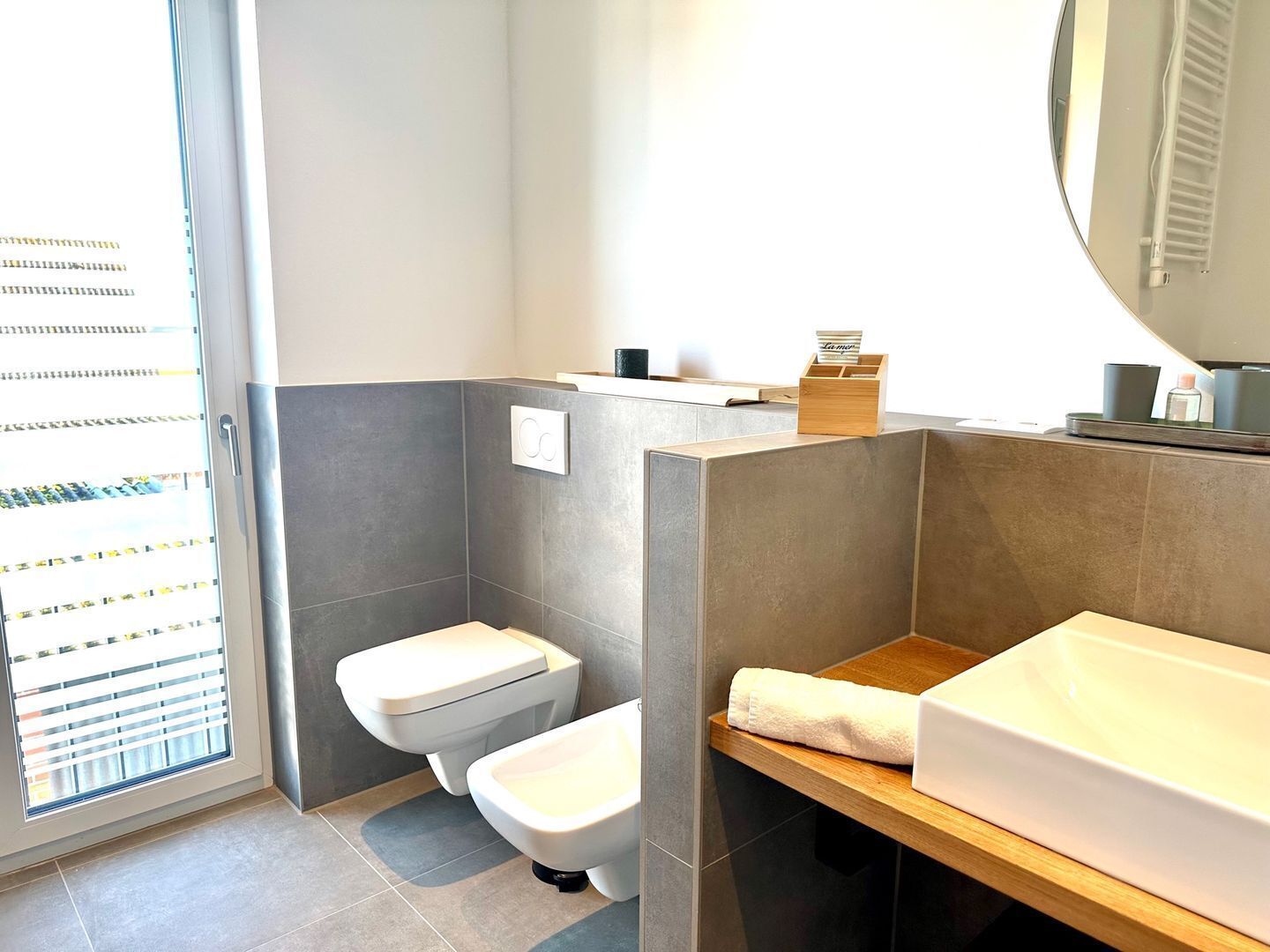 A modern bathroom with a toilet, bidet, and a sink with a wooden countertop.