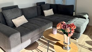 Ein modernes Wohnzimmer mit einem grauen Ecksofa, einem kleinen runden Couchtisch und einer Vase mit Blumen.