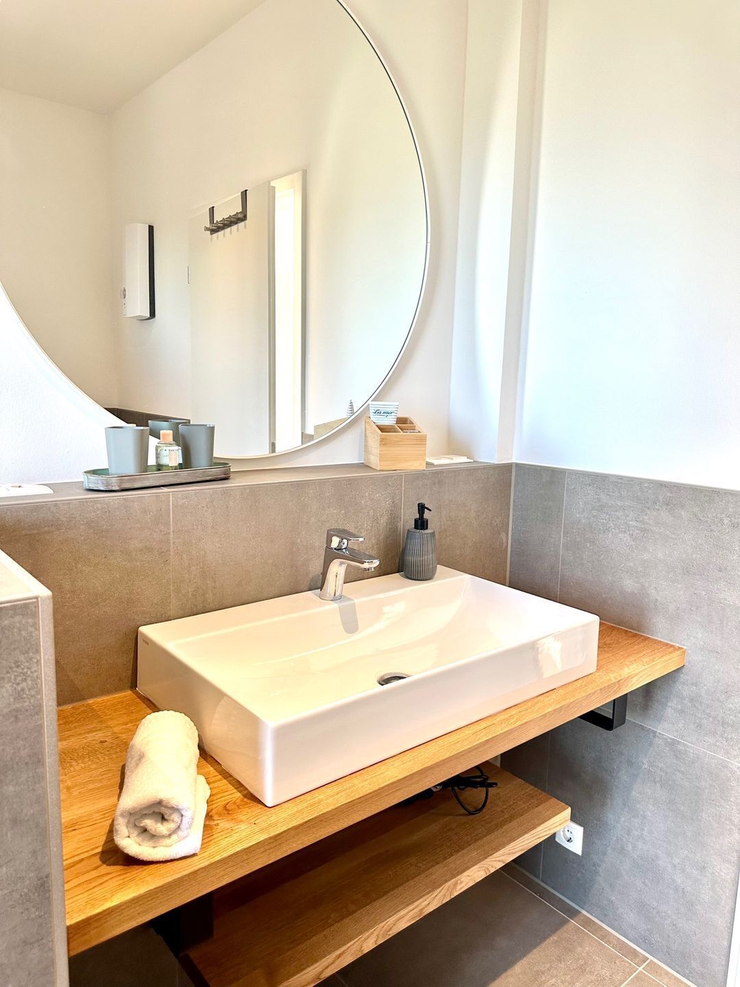 Une salle de bain moderne avec un lavabo rectangulaire, un meuble-lavabo en bois, un grand miroir et une serviette posée sur le comptoir.