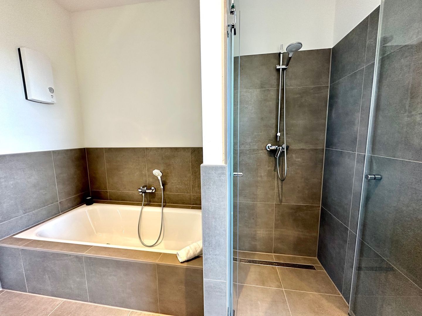 A modern bathroom with a bathtub, a shower with a handheld showerhead, and a glass-enclosed shower stall.