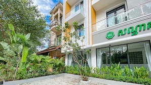 A modern building with a green sign, surrounded by lush greenery and a tiled courtyard. - ANGKOR SIVUTHA HOTEL (Siem Reap)