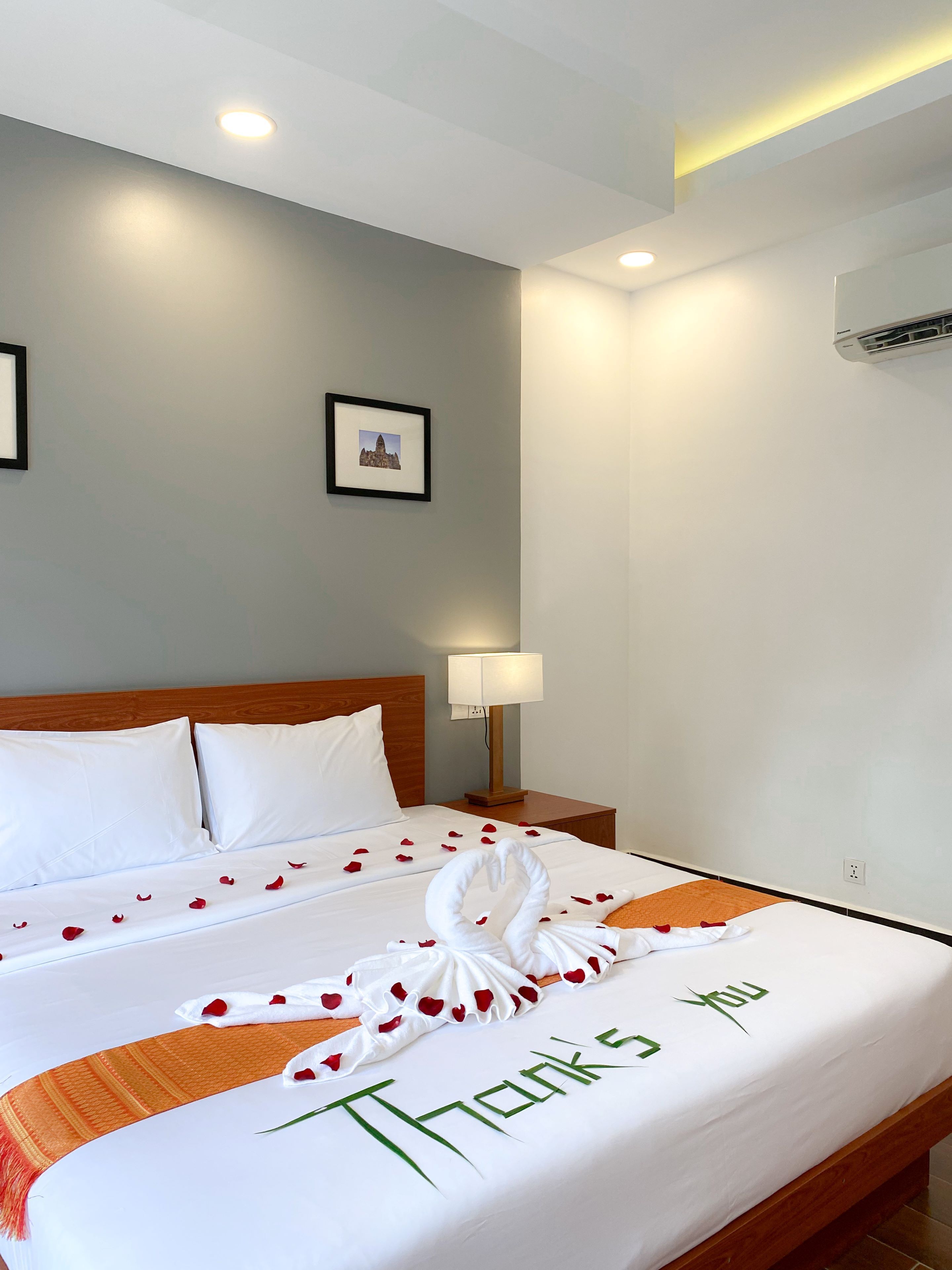 A neatly made bed with a 'Thank You' message, white pillows, and rose petals.