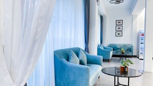 A modern living room with a blue sofa, a round glass coffee table, and a small table with a plant. - ANGKOR SIVUTHA HOTEL (Siem Reap)