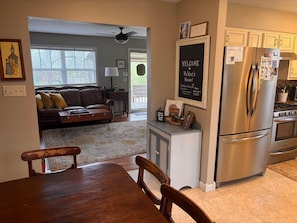 A kitchen with a stainless steel refrigerator, a dining table with chairs, a sofa in the adjacent living room, and a 'WELCOME to Walters House!' sign. - Downtown Cotter Retreat -- Great Outdoor Space!! 200 feet of String Lights! (Cotter)