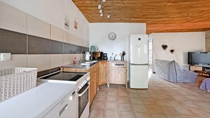 Een moderne keuken met een fornuis, spoelbak en koelkast, houten keukenkastjes, en een eethoek met een televisie.