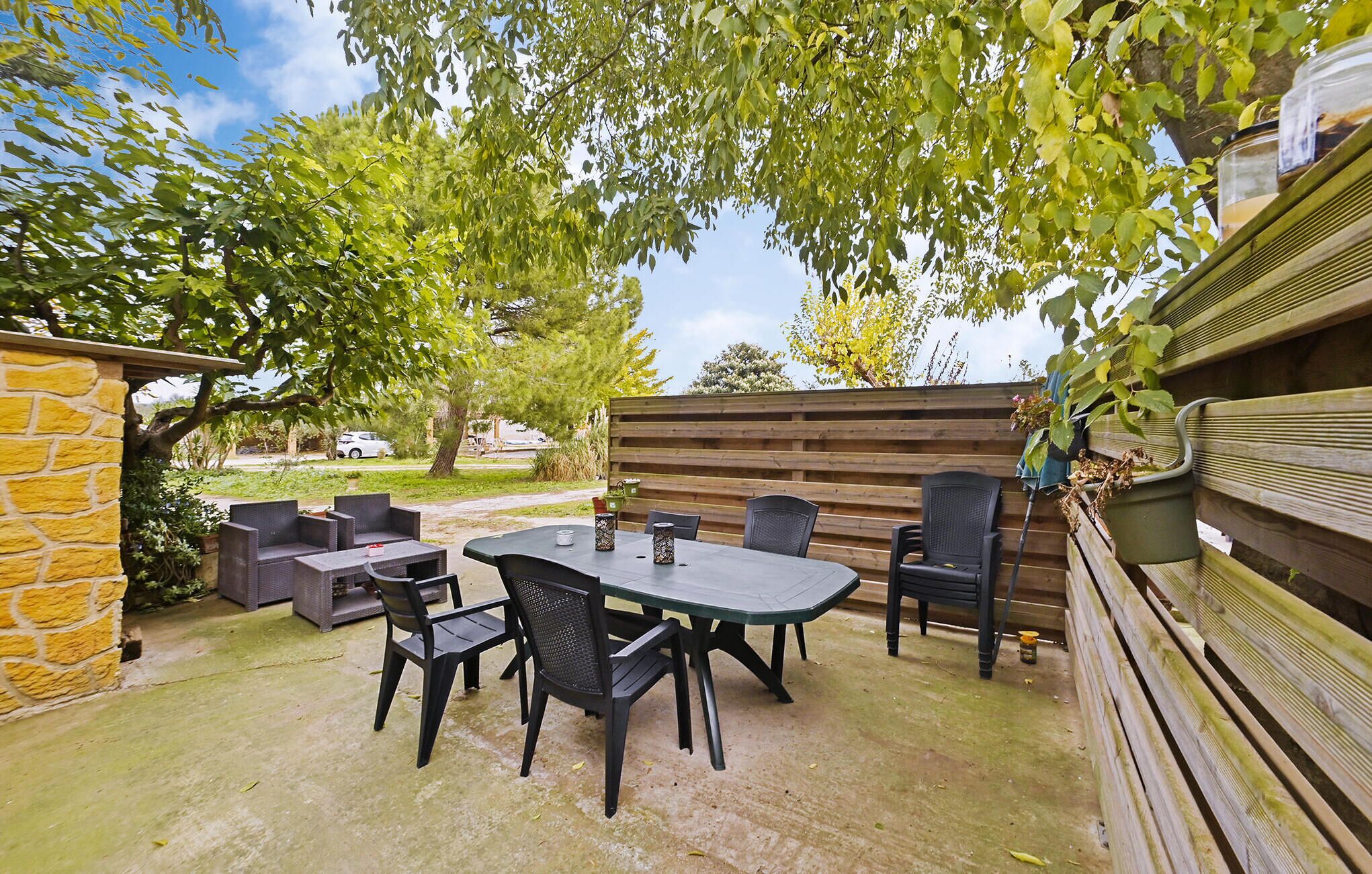 An outdoor patio with a table and chairs, surrounded by a stone wall and wooden fence.