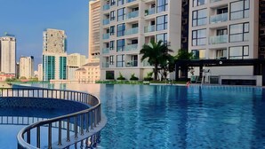 Un immeuble résidentiel moderne doté d’une piscine, avec des balcons pourvus de garde-corps en verre offrant une vue dégagée sur le paysage urbain environnant.