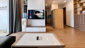 Un salon moderne avec un téléviseur à écran plat, une table basse, un canapé et, au fond, un coin cuisine.