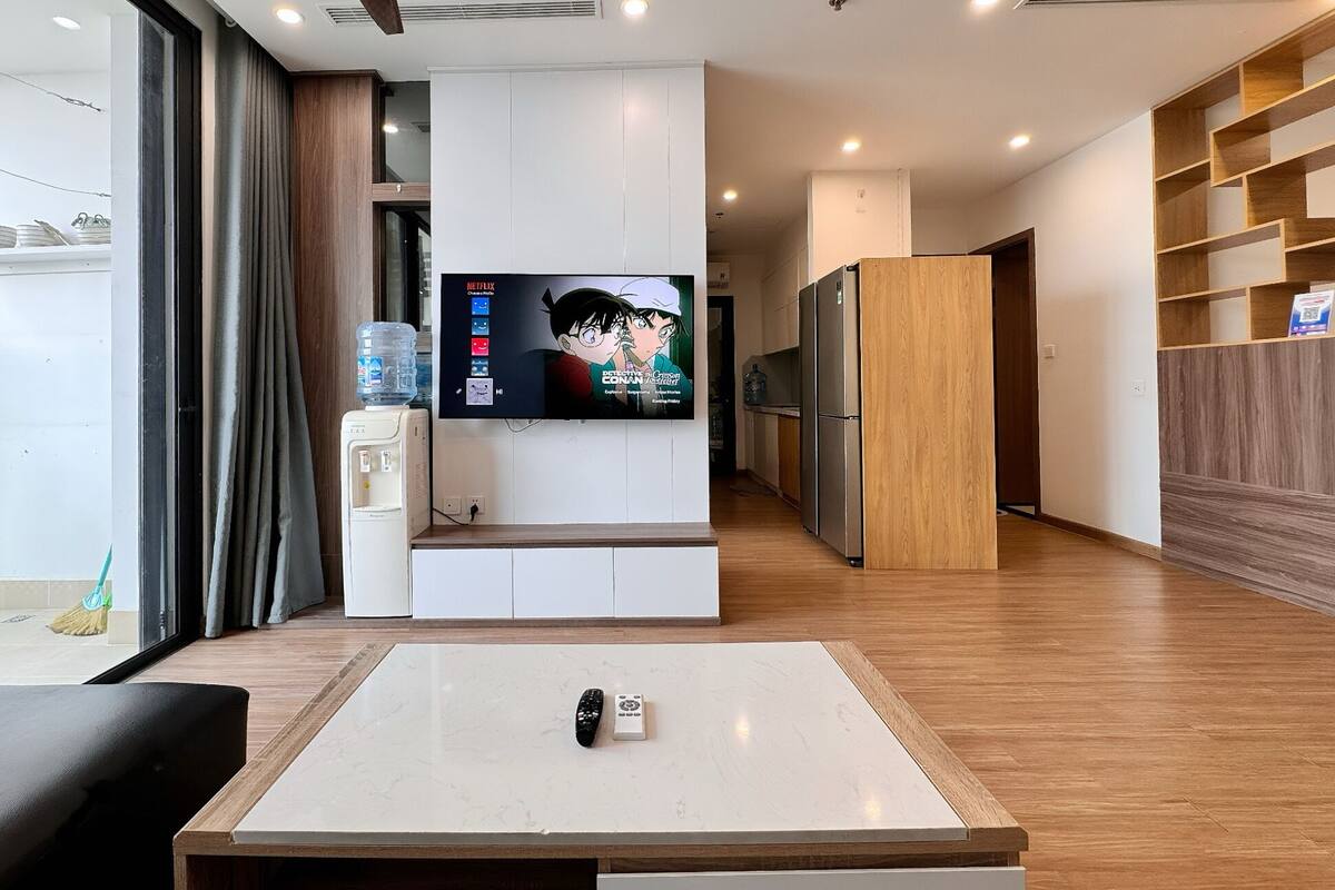 Un salon moderne avec un téléviseur à écran plat, une table basse, un canapé et, au fond, un coin cuisine.