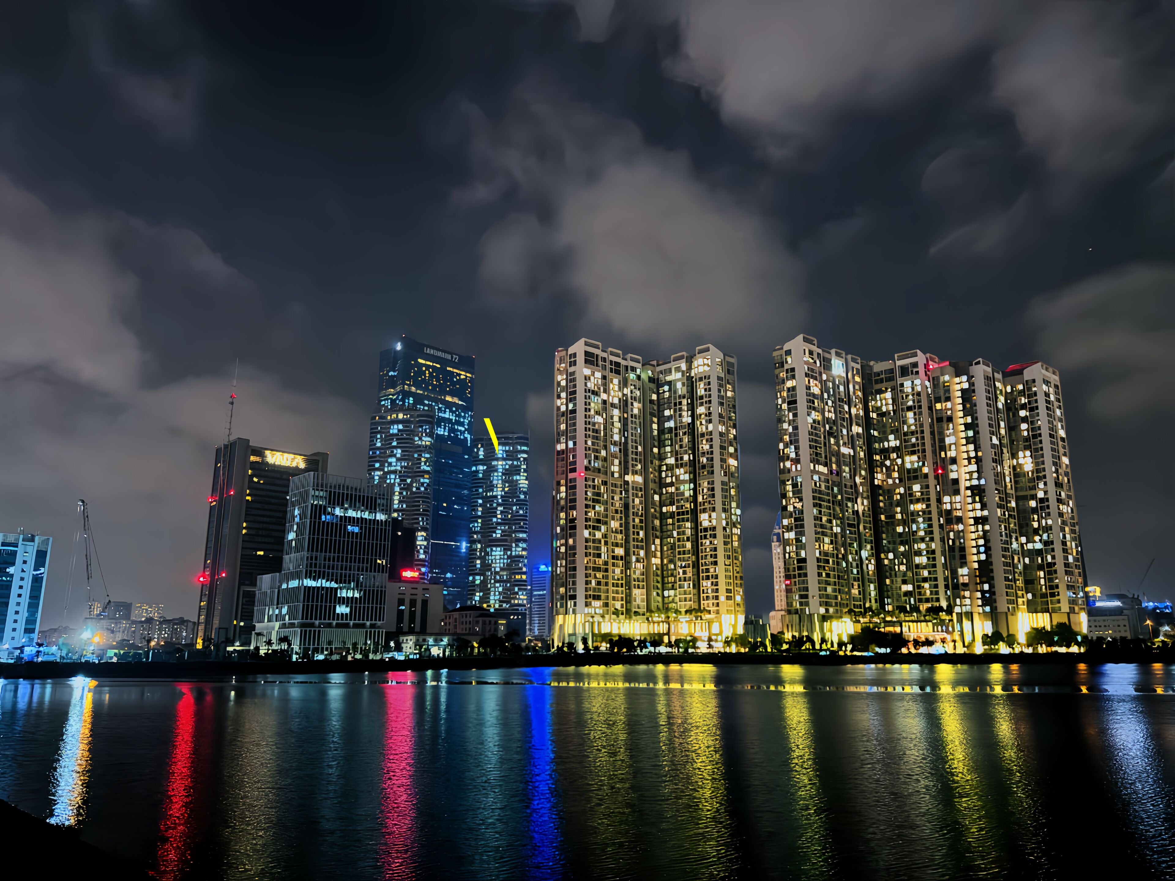 A nighttime cityscape with high-rise buildings reflecting on a body of water.