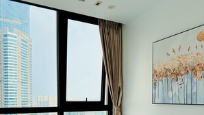 Une chambre d’hôtel dotée d’une grande fenêtre donnant sur la ville, d’un lit avec du linge de maison blanc et d’un tableau représentant des arbres et des oiseaux, accroché au mur.