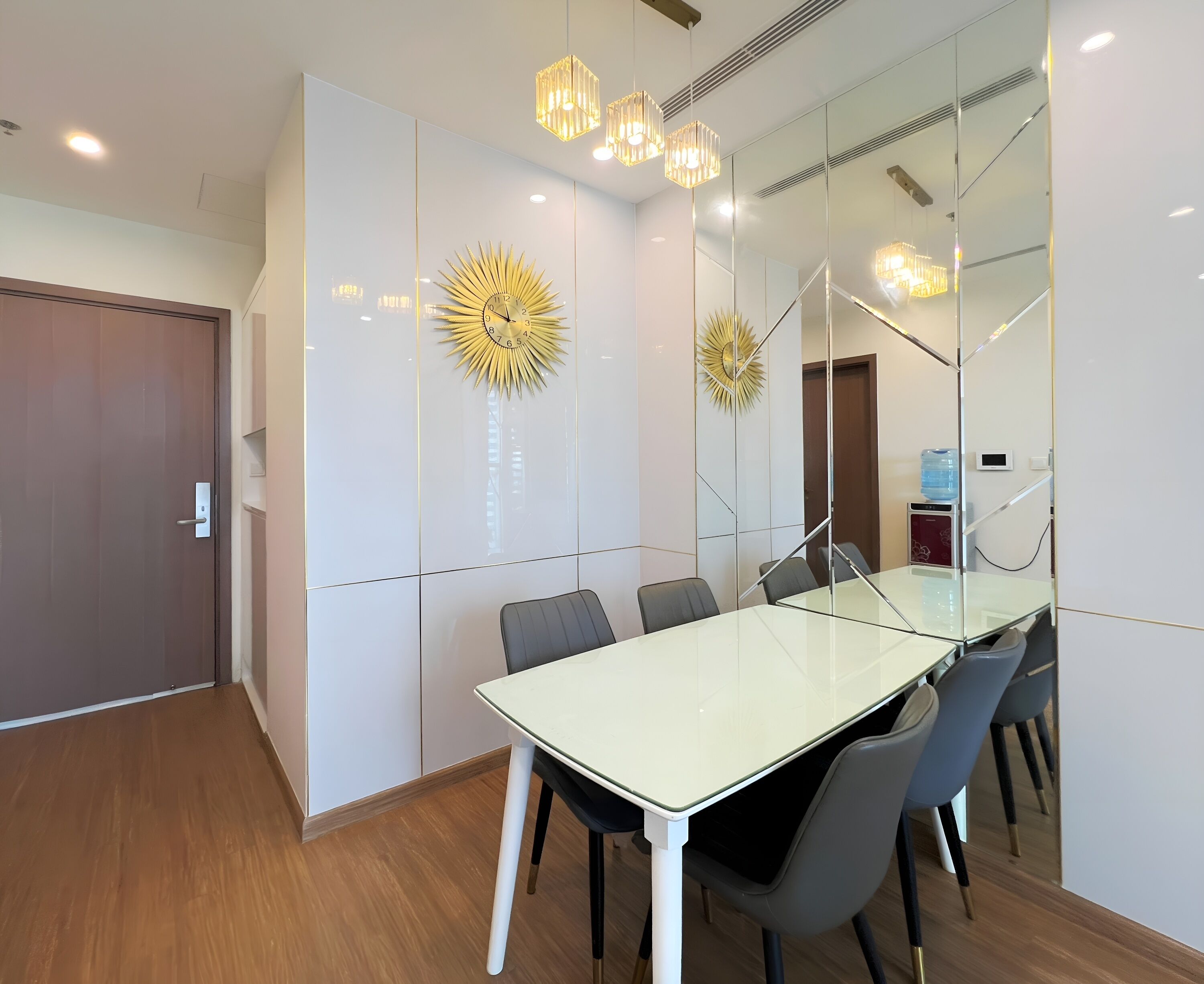 Una sala de conferencias moderna con una mesa de vidrio, sillas grises y relojes decorativos en la pared.