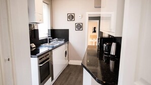 A compact kitchen with a dishwasher, oven, and a coffee machine. There are two framed inspirational quotes on the wall. - 4 Bed House, Sleeps 9, Free Parking (Stoke-on-Trent)