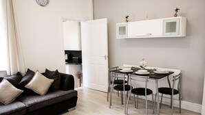 A modern living room with a dark grey sofa, a dining table with four chairs, and a white cabinet above the table. - 4 Bed House, Sleeps 9, Free Parking (Stoke-on-Trent)