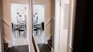 A hallway leading to a dining area with a table set for four, chairs, and a clock on the wall. - 4 Bed House, Sleeps 9, Free Parking (Stoke-on-Trent)