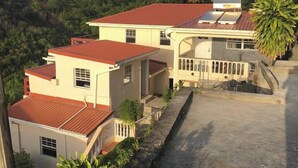 A residential area with houses featuring red roofs and light-colored walls, surrounded by lush greenery and hills. - Story Villa, 2 Bedrooms with Mountain & Ocean View (Canaries)