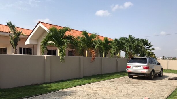 A residential area with a paved driveway, a white car parked on the street, and a bag of cement on the grass. - 3 Bed House - Sleeps 9 - Pets - Garden - Parking (Accra)