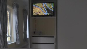 Hotelkamer met een bed, een televisie aan de muur, een raam met gordijnen en een nachtkastje.