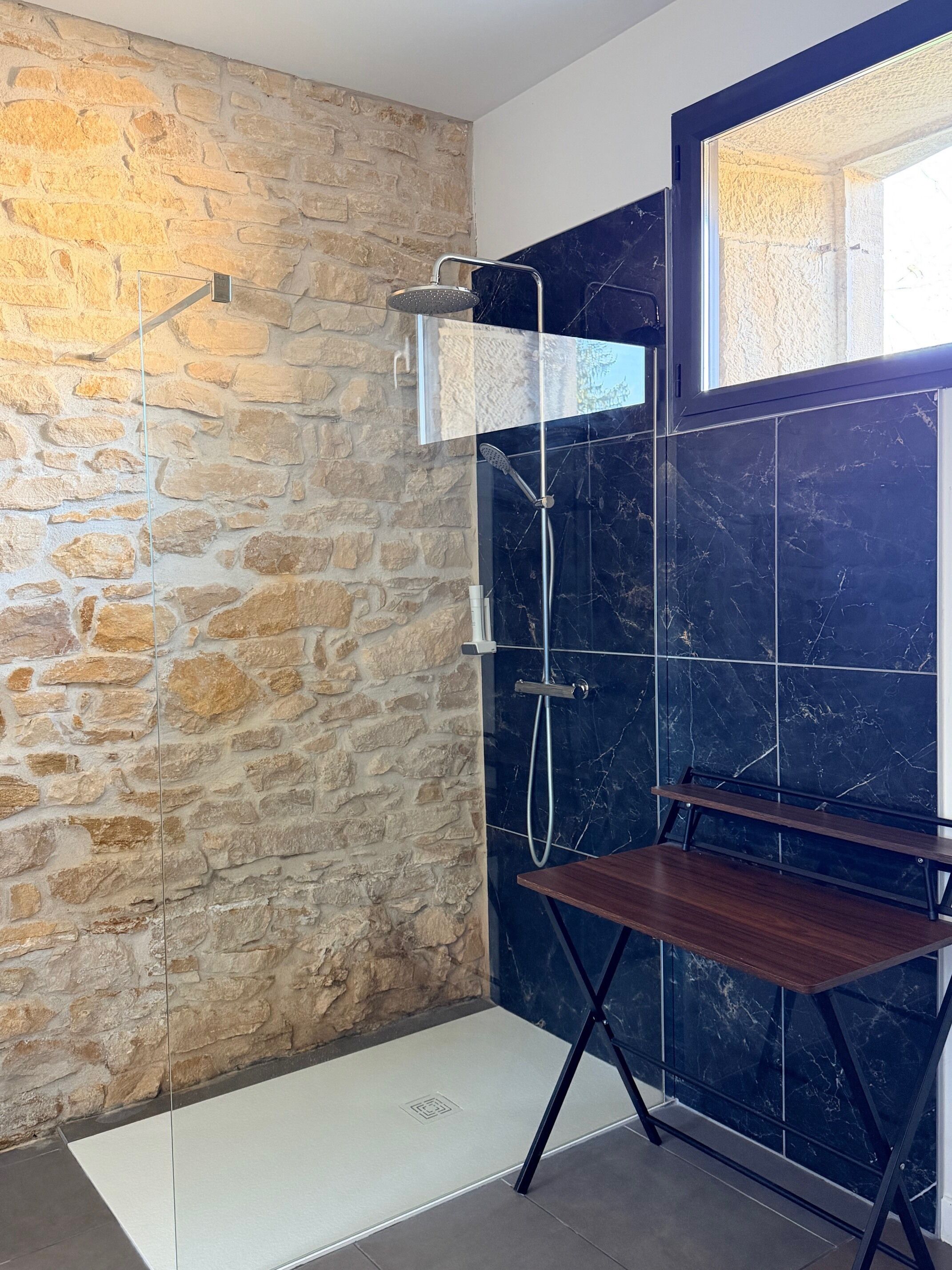 A modern bathroom with a stone wall, a black marble shower, and a wooden bench.
