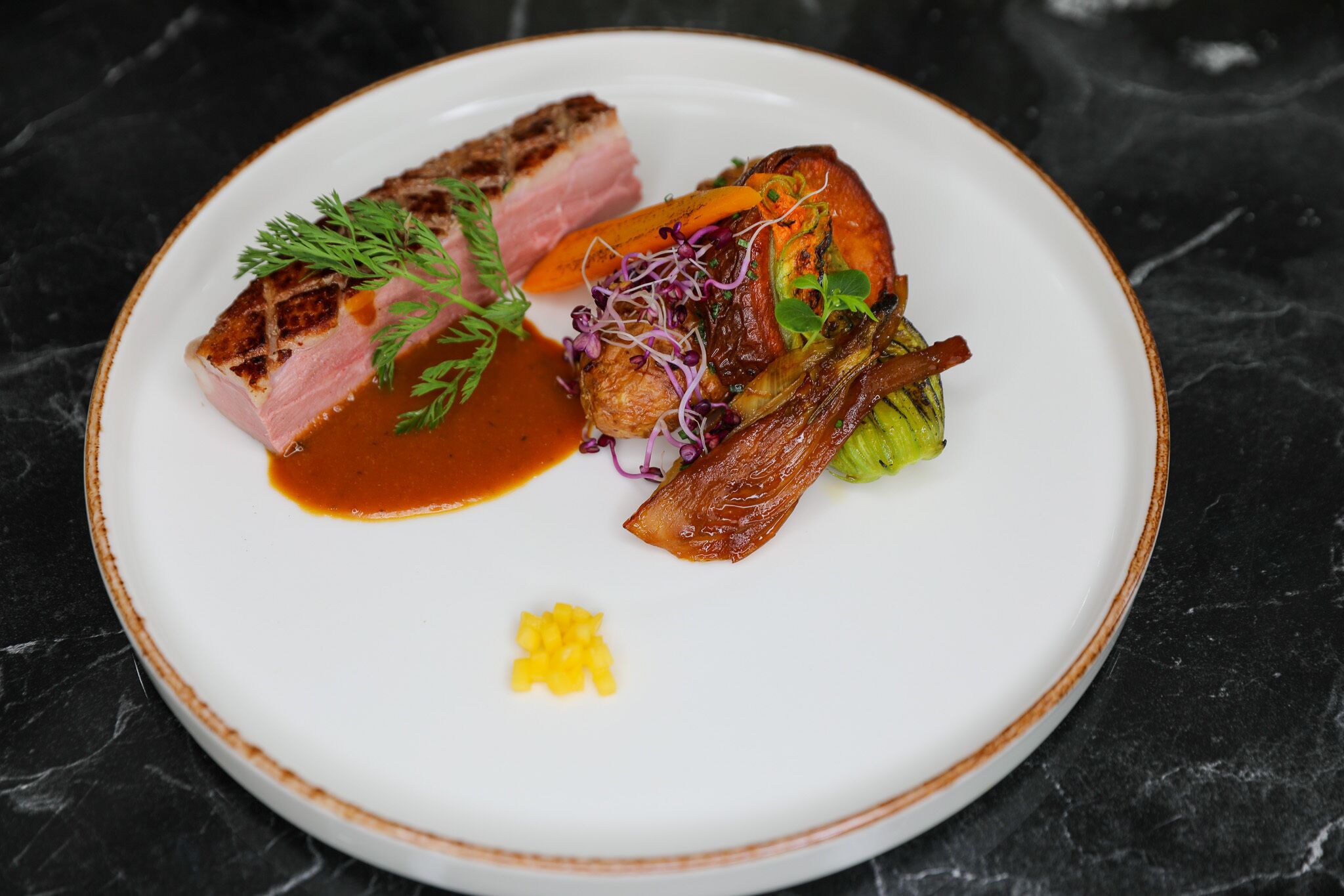 A white plate with a variety of food items including a piece of meat, vegetables, and a small amount of sauce.