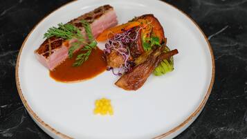A white plate with a variety of food items including a piece of meat, vegetables, and a small amount of sauce.