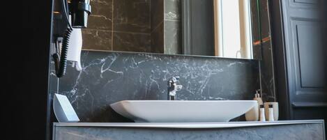 Un baño moderno con un espejo grande, un lavamanos blanco y un secador de pelo en la pared.