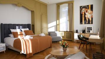 Habitación de hotel con cama, escritorio, silla, sofá, mesita de noche y ventana con cortinas.