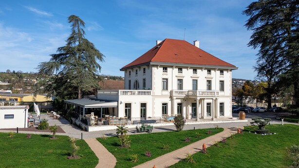 Un edificio grande, su due piani, con tetto rosso e pareti bianche, dotato di una zona salotto esterna coperta e di un prato curato con un vialetto.